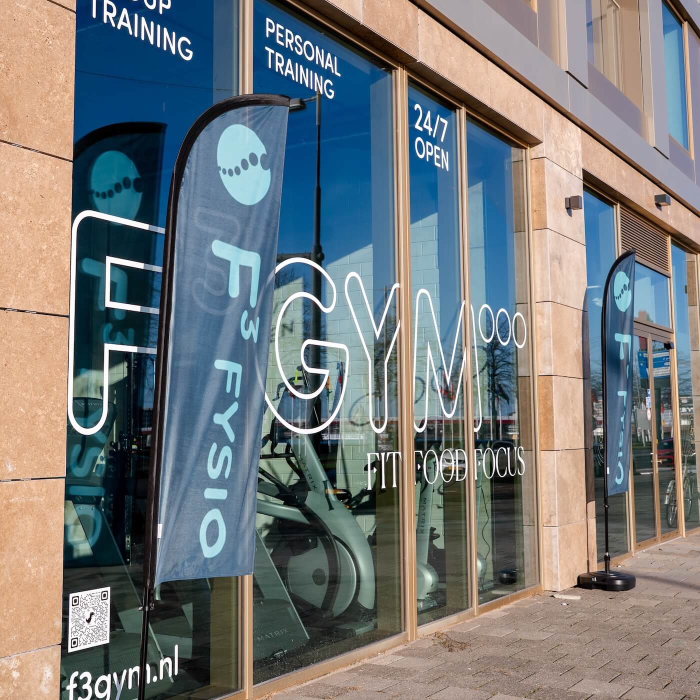 Entree van F3 GYM aan de Hertekade met banners voor personal training en 24/7 open